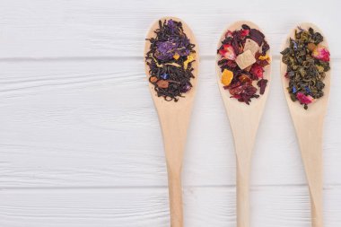 Ahşap arka plan üzerinde farklı çay yaprakları ile Kaşıklar.