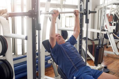 Spor salonunda ağırlık kaldıran yalancı yaşlı adam.