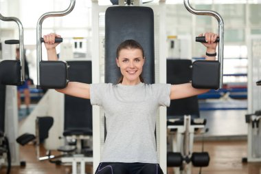 Woman on shoulder press machine in fitness club.