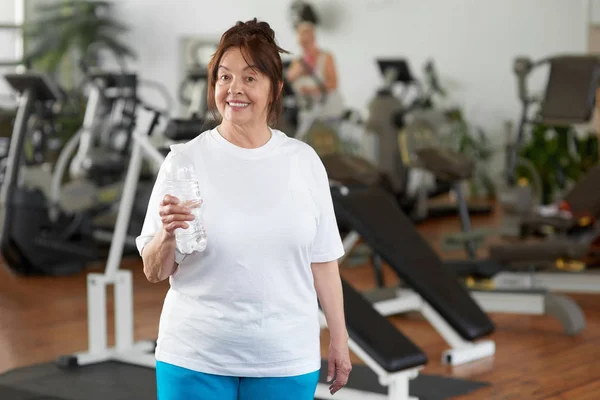 Happy mature woman with water at gym. — Stock Photo, Image