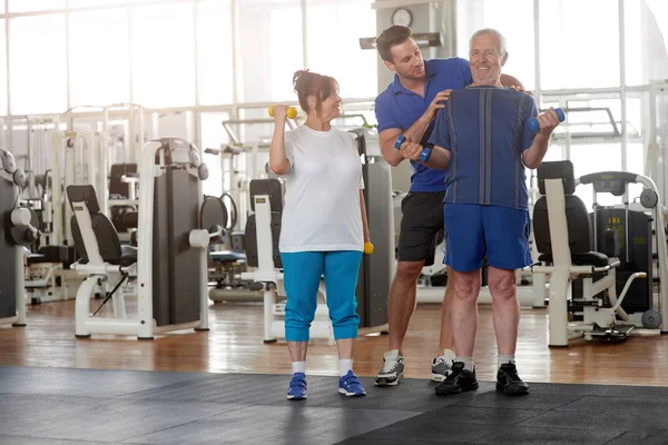 Personal trainer helping lift dumbbells to seniors.
