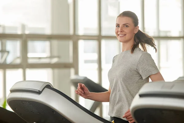 Mujer joven usando una cinta de correr en un gimnasio . — Foto de Stock