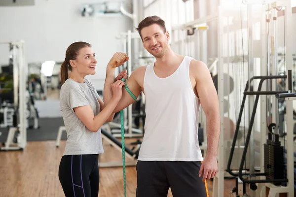 Woman measuring athletics man biceps.