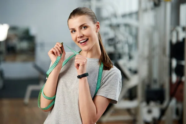 Happy delighted woman with measuring tape at gym.