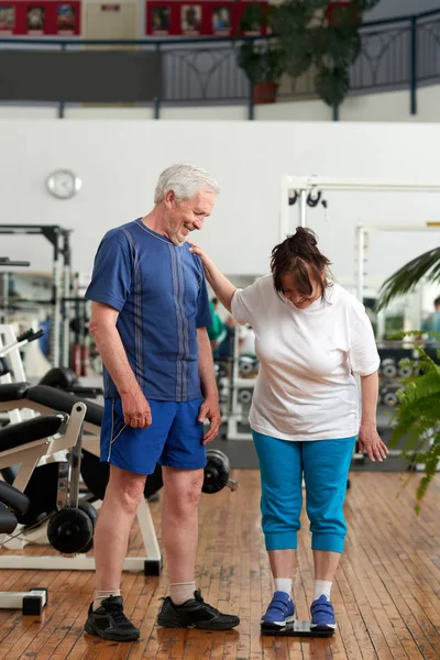 Senior woman stands on weight scale at gym.