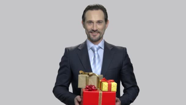 Businessman holding gift boxes on gray background. — Stock Video