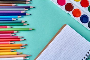 Suluboya paleti, eskiz defteri ve çok renkli kalemler.