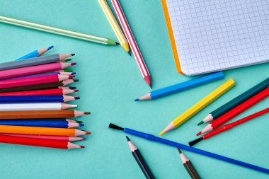 Boş çizim defteri ve renkli arka plan üzerine dağınık kalemler.