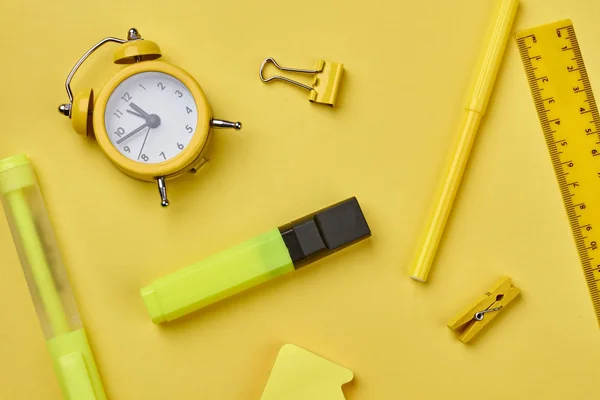 Reloj despertador y útiles escolares sobre fondo amarillo . — Foto de Stock