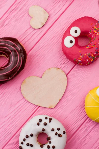 Donuts e corações de madeira no fundo de cor . — Fotografia de Stock