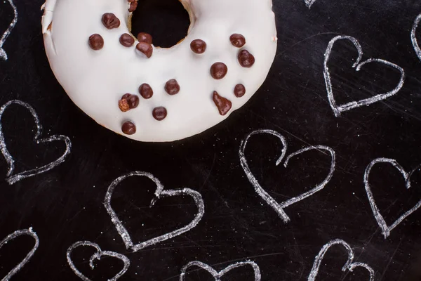 White donut and drawn hearts on black background.