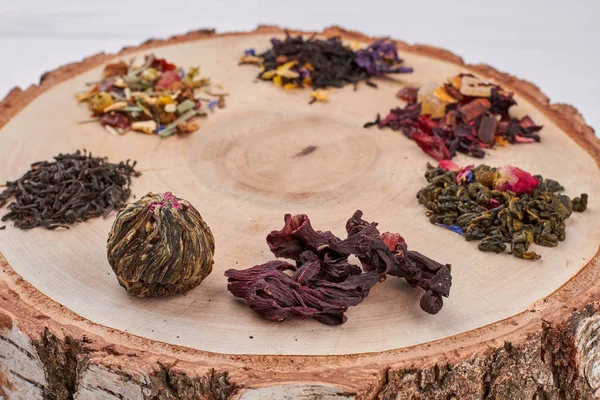 Different types of dry tea on tree slice. — Stock Photo, Image