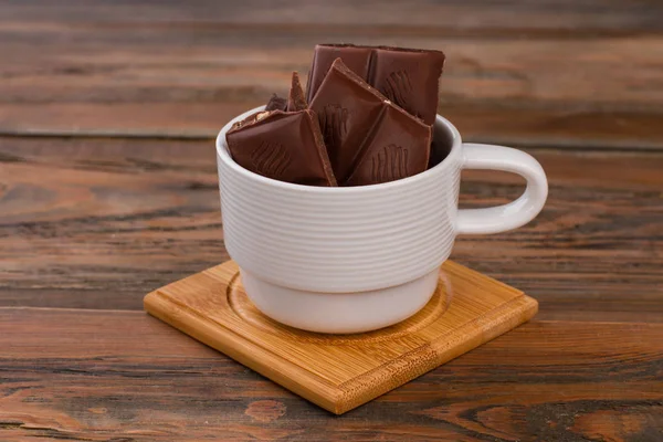 Tasse mit Schokoladenstücken auf Holzgrund. — Stockfoto