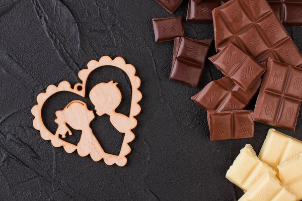 Chunk de chocolate e coração de madeira em fundo preto . — Fotografia de Stock