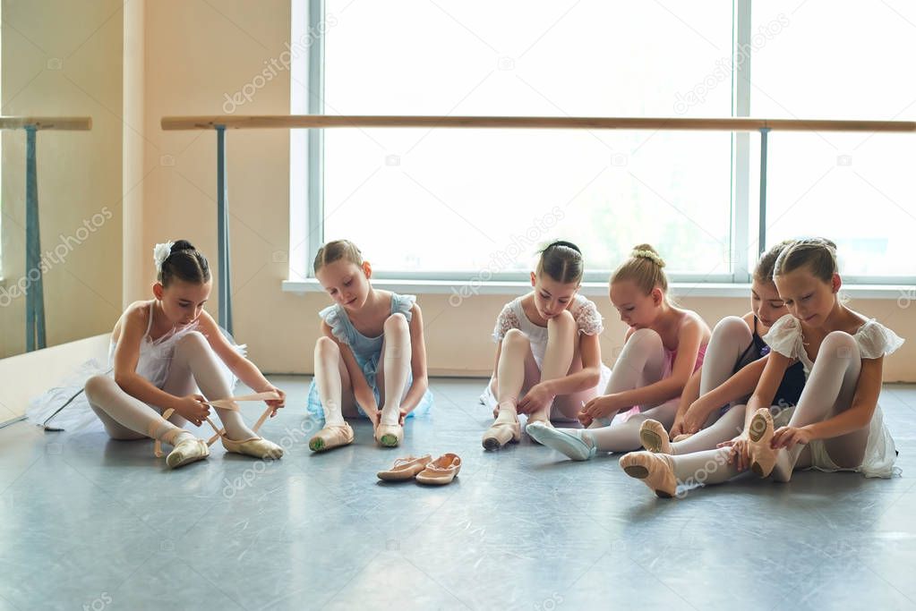 Young ballerinas putting on shoes in studio.