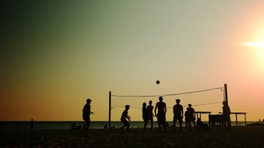 Bir grup genç plajda voleybol oynuyor..