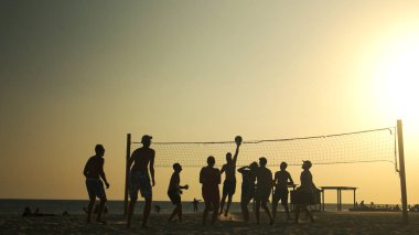 İnsanlar gün batımında plajda voleybol oynuyorlar..