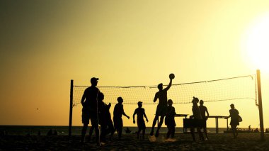 Gün batımında plaj voleybolu oynayan insanların siluetleri.