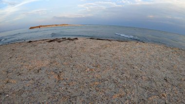 Kumlu plaj, deniz dalgaları ve mavi gökyüzü.