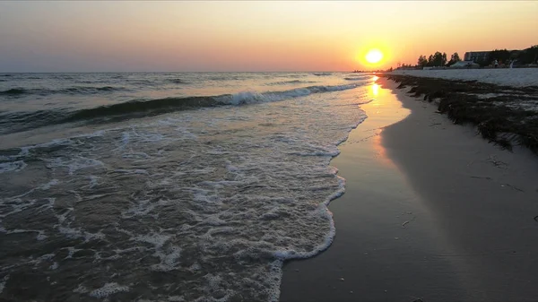 Turuncu güneş ve köpüklü dalgalar ile plaj gün batımı. — Stok fotoğraf