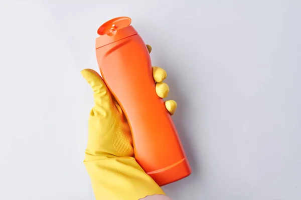 Main dans le gant tenant détergent bouteille orange . — Photo