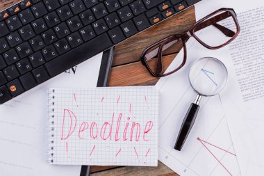 Tahta zemin üzerinde büyüteç, gözlük ve klavye ile üst görünüm not defteri.