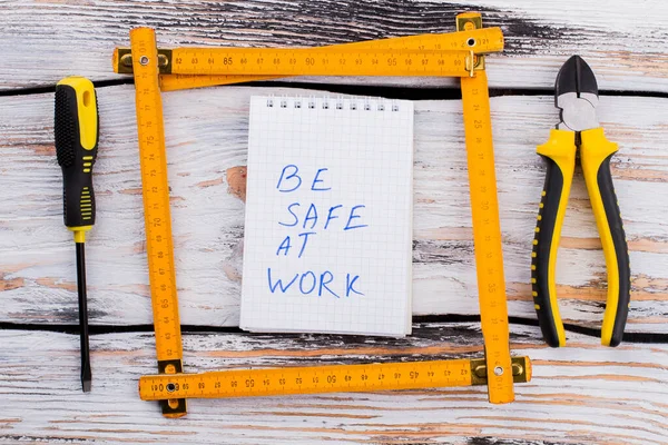 Be safe at work note in a ruler frame on white wooden table.