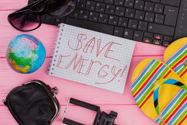 Save energy on notebook with womans traveler accessories glasses wallet and flip-flops on pink table top background.