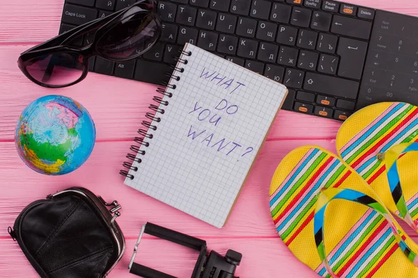 What do you want on notebook with womans traveler accessories glasses wallet and flip-flops on pink table top background.