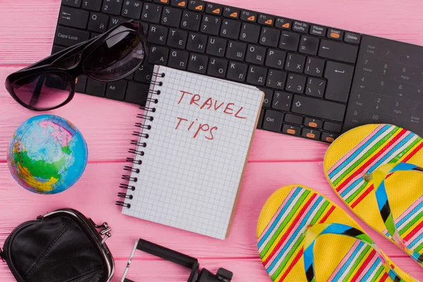 Travel tips on notebook with womans traveler accessories glasses wallet and flip-flops on pink table top background. — Stock Photo, Image