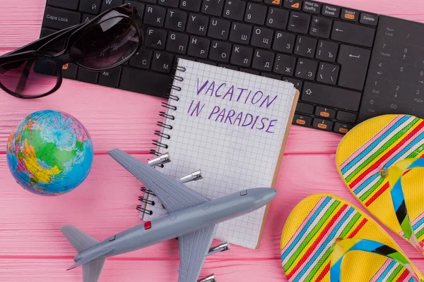 Vacation in Paradise on notebook with womans traveler accessories glasses wallet and flip-flops on pink table top background. — Stock Photo, Image