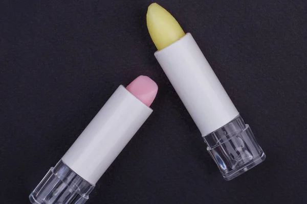 Pink and yellow lipstick in white tube on black background. — Stock Photo, Image