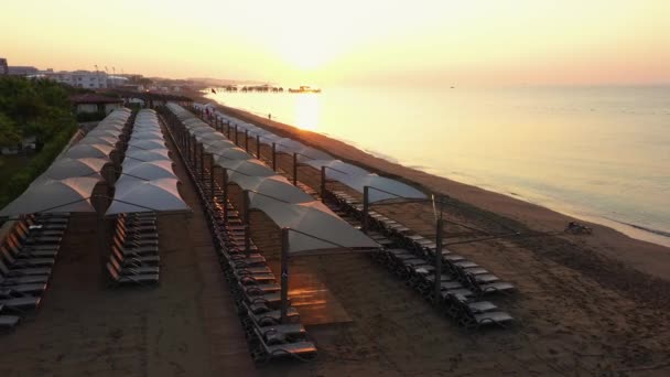 Widok na piaszczystą plażę z leżakami o zachodzie słońca. — Wideo stockowe