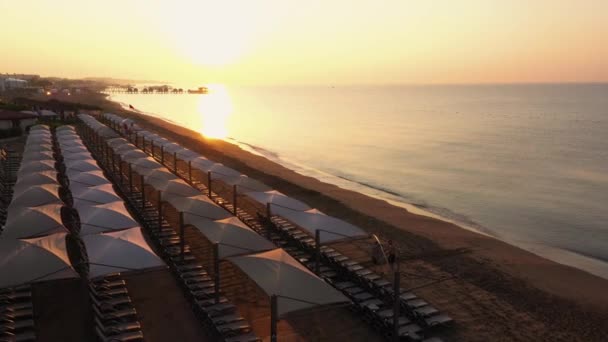 Vista superior de tumbonas en la playa de arena vacía al atardecer . — Vídeo de stock