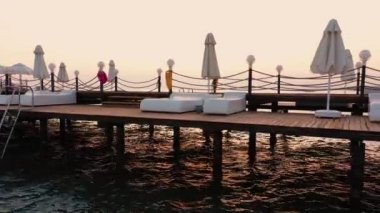 Güneşli yataklı ahşap iskele ve denizde şemsiyeler.