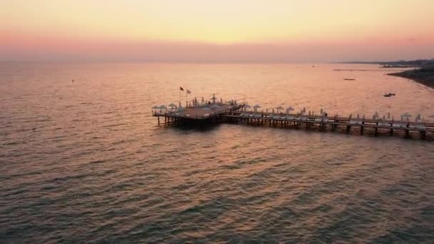 Vue par drone d'une jetée en bois au bord de la mer au coucher du soleil. — Video