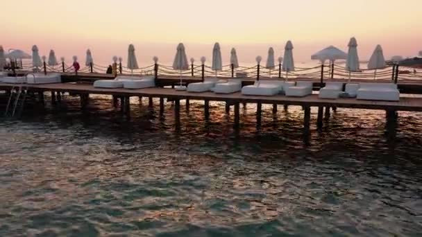 Jembatan kayu dengan tempat tidur matahari di laut saat matahari terbenam. — Stok Video
