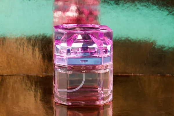 Transparent pink perfume bottle on a reflective surface. — Stock Photo, Image