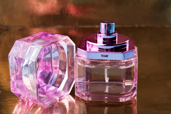Pink glass perfume bottle on a reflecting surface.