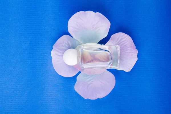 La botella poco transparente del perfume femenino sobre los pétalos de flores . — Foto de Stock
