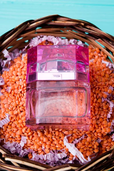 Frasco rosa transparente de perfume en la cesta de las lentejas . — Foto de Stock