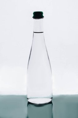 Beyaz arka planda yansıması olan dolu bir su şişesi.