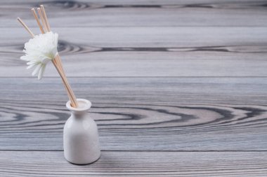 Yapay çiçekli ve tahta sopalı beyaz vazo..