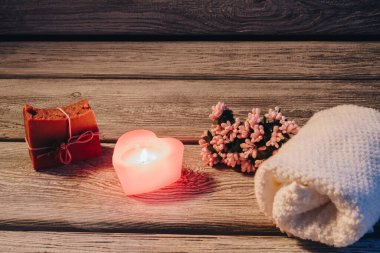 Ahşap arka planda kalp şeklinde mum ve spa aksesuarları olan spa kompozisyonu.
