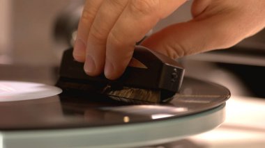 Gramofon iğnesini tutan elin yakın görüntüsü.