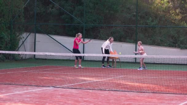 Instructor enseñando a los niños a jugar tenis en la cancha al aire libre . — Vídeos de Stock