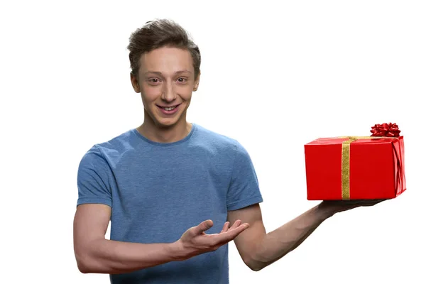 Retrato de sorrindo adolescente menino mostrando caixa de presente vermelho com arco dourado . — Fotografia de Stock