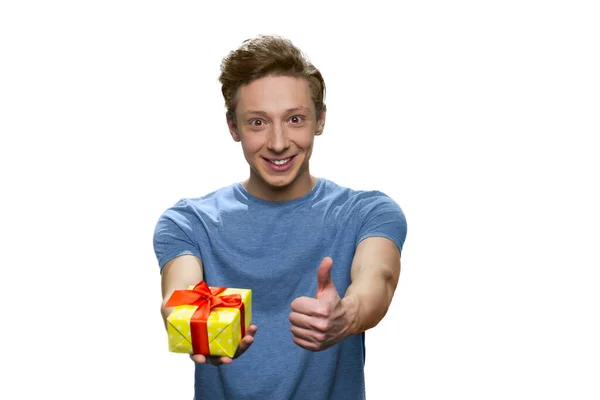 Chico joven emocionado con caja de regalo amarilla mostrando el pulgar hacia arriba . — Foto de Stock