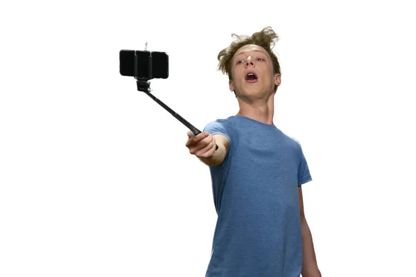 Adolescente menino está segurando selfie vara com smartphone e posando . — Fotografia de Stock