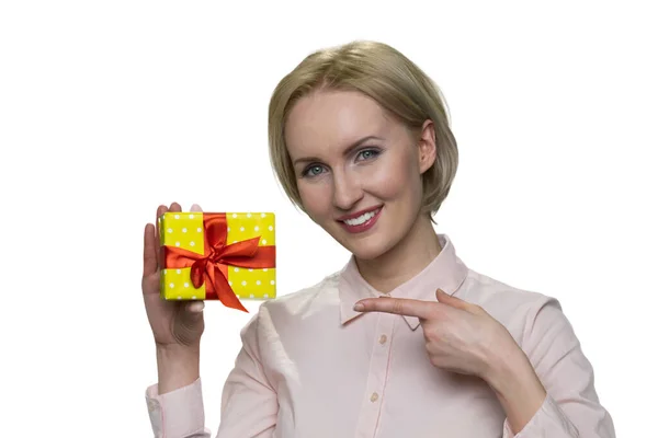 Mulher loira feliz em blusa segurando pequena caixa de presente em sua uma mão e apontando para o presente por dedo . — Fotografia de Stock